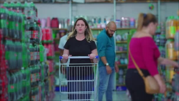 食料品店の通路で買い物客とショッピングカートを押す女性は 食料品店での消費者主義の習慣を描いた — ストック動画