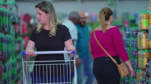 棚の上の製品のためのスーパーマーケットの通路ブラウジングで買い物客 食料品店で商品を探すショッピングカートを押す女性消費者 — ストック動画