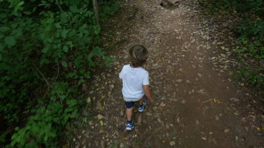 Yeşil patikada yürüyüş yapan çocuk ormanda dışarıda yürüyor.
