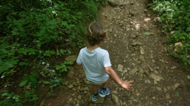 Çocuk doğada yeşil yolda koşuyor. Ormanda yürüyüş yapan küçük, sportif çocuğun yukarıdan bakışı.