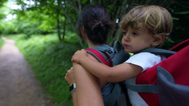 Anne, oğlunu sırt çantasında taşıyor anne doğada çocukla yürüyüşe çıkıyor.