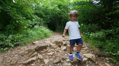 Aktif bir çocuk ormanda koşuyor, dağlarda yürüyüş yapıyor.