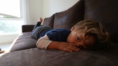 Küçük bir çocuk kanepede uzanıyor. Dalgın bir çocuk kanepede yatıyor.