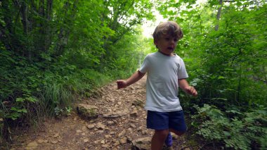 Yeşil patikada yürüyüş yapan çocuk ormanda dışarıda yürüyor.