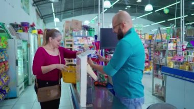 Kadın alışverişçi, çıkış noktasında erkek çalışanla etkileşim halinde olan ürünleri tarıyor. Brezilya Market Ürün satın alma sahnesi
