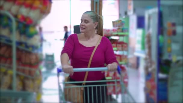 슈퍼마켓에서 쇼핑을 중년의 여성들 선반에 상품들을 둘러보는 통로를 있습니다 — 비디오