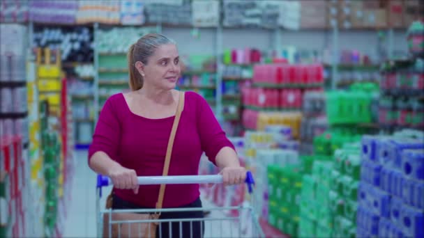 女购物者推着购物车在超市过道里走着 浏览描绘消费主义生活习惯的产品 中年女性消费者 — 图库视频影像