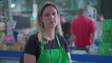 Marketteki kasiyerin kadın çalışanının portresi. Arka planda müşteriler var. Marketin ciddi kadın çalışanları.