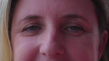 Kameraya gülümseyen orta yaşlı neşeli bir kadının makro yakın çekimi. Kafkasyalı bir kadın yüzü ve gözleri kırışıklıklarla sımsıkı kapatıyor, olgunlaşmış yaşlanıyor.