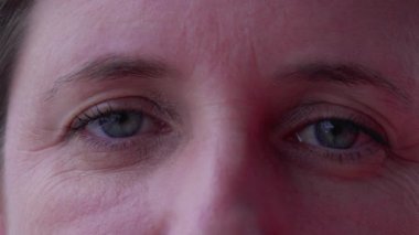 40 'lı yaşlarda, kameraya bakan mavi gözlü bir kadının makro yakın çekimi. Yüzünde kırışıklıklar ve ciddi ifade olan beyaz bir kadın.