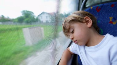 Düşünceli bir çocuk otobüse binip pencereye yaslanır.