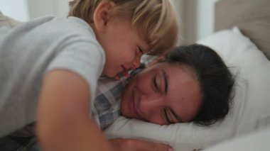 Küçük çocuk sabah annesini uyandırıyor, annesine atlıyor ve öpüşüyor.