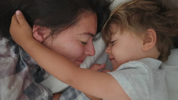 Mother child love and affection in morning bed waking up little boy loving mom family moment