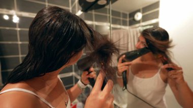 Kadınlar saçlarını banyo aynasının önünde kurutur.