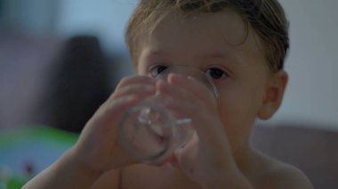 Su içen küçük çocuk bir bardak su içiyor.