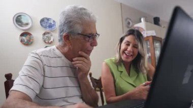 Mutlu olgun insanlar dizüstü bilgisayarın önünde kendiliğinden gülüyor ve gülümsüyor. Yaşlı çiftler arasında gerçek hayattaki neşeli etkileşimler kahkahalar atıyor.