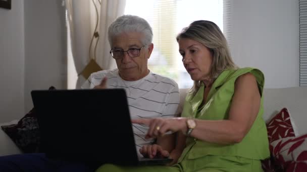 成熟したカップルは 自宅のソファーで座ったラップトップの前に座って モダンな技術を一緒に従事しました 既婚の夫と妻が屋内コンピュータ画面を見つめている — ストック動画