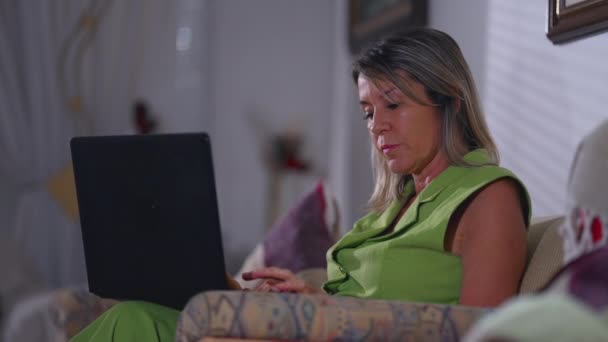 集中した上級女性は 夕方に自宅のソファーに座っているラップトップコンピュータにタイピングします 現代技術に従事する高齢女性の白人 電子メールを構成する — ストック動画