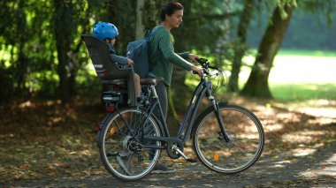Anne ve baba, bisikletin arka koltuğunda çocuklu bisiklet taşıyor.