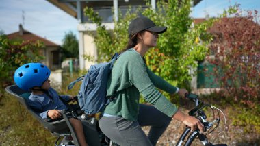 Bisikletli anne dışarıda, yeşil yolda çocukla bisiklet sürüyor.