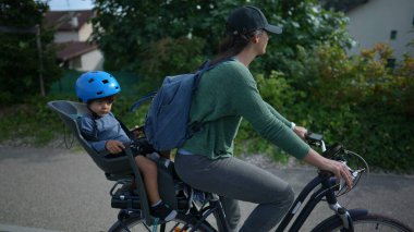 Bisikletli anne arka koltukta çocukla dışarıda bisiklet sürüyor.
