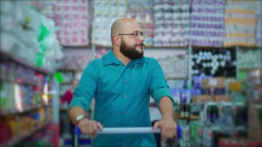 Marketteki alışveriş arabalarını iten bir erkek, markette tüketici yaşam tarzı alışkanlıklarını tasvir eden ürünleri raflarda arıyor.