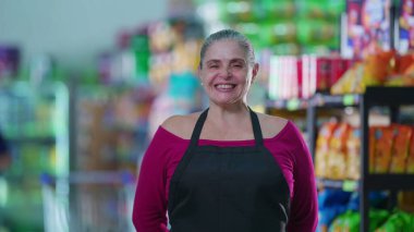 Marketin neşeli kadın çalışanı önlük giyiyor ve kameraya gülümsüyor. iş gücü personeli çalışanı