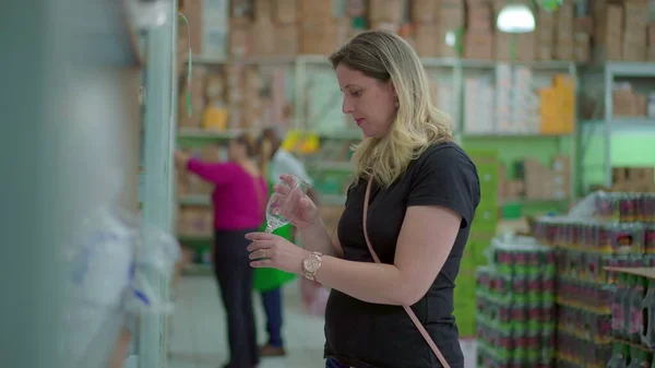 Woman picks up glass at grocery store, inspects product at store aisle from shelf, consumer lifestyle habits