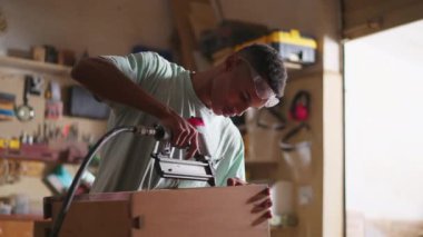 Genç bir siyah marangoz, marangozluk atölyesinde mobilya tamir ediyor. Tahta obje yapmayı öğrenen çırakların mesleği, sondaj ekipmanları kullanmak.