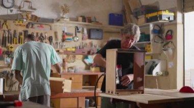Marangoz sahnesinde iki marangoz ahşap mobilya yapmak ve tamir etmek için aletlerle çalışıyor.