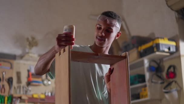 快乐的年轻木匠在木片上涂胶水 在木工车间工作 学徒专心于他的工作 用专注的表情粘贴物体 — 图库视频影像