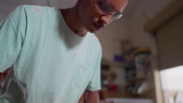 Ένας Εστιασμένος Νεαρός Μαύρος Ξυλουργός Κουρεύει Ξύλο Στο Εργαστήριο Συγκεντρωμένη — Αρχείο Βίντεο