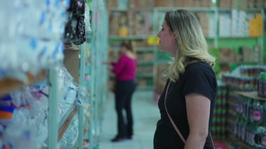 Marketin rafında kadın alışveriş ürünleri var. Kadın süpermarkette tüketici yaşam tarzlarını tasvir eden şeyler arıyor