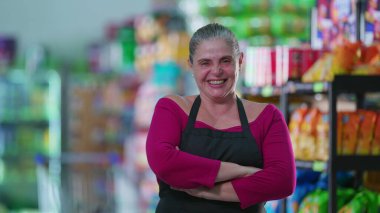 Neşeli Kadın Market İşçisi Kameraya gülümseyen, kollarını kavuşturan, önlük takan