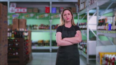 Süpermarketin kadın çalışanları ürün envanterinin yanında duruyor ve kolları çapraz ve ciddi ifadeleri var. Kadın çalışanın sert duyguları