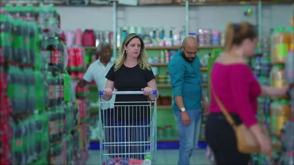 stock image Woman pushing shopping cart at grocery store aisle with shoppers in background depicing consumerism habits at grocery store