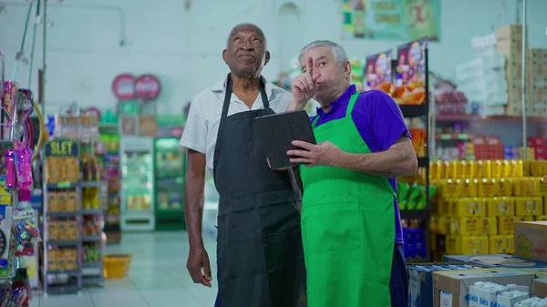 Dwóch Starszych Zróżnicowanych Pracowników Pracujących Supermarkecie Przyglądających Się Tabletom Scena — Zdjęcie stockowe