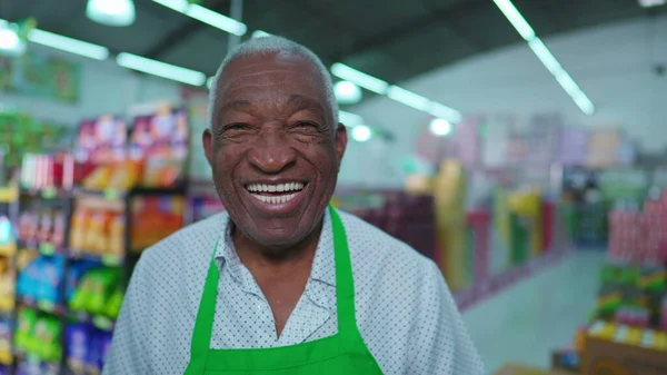 One joyful black senior staff of supermarket smiling at camera standing inside Grocery Store aisle with friendly charismatic expression
