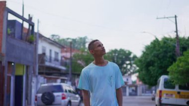 Düşünceli, genç, siyah Brezilyalı bir adam dalgın ve düşünceli bir ifadeyle gökyüzüne bakıyor. Güney Amerikalı 20 'li yaşlarda mahalleye bakan biri.