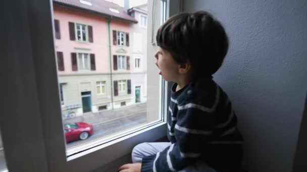 子供は家の窓に呼吸し 凝縮を生み出し 2階建物からガラスに息を吹き込む 退屈な子供 — ストック動画