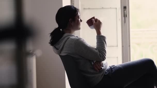 Przemyślana Kobieta Sączy Ciepły Napój Patrząc Przez Okno Balkonu Kontemplacji — Wideo stockowe