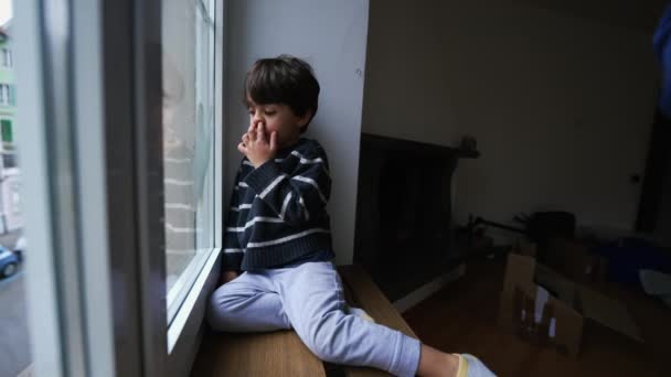 アパートから外を見ながら家の窓に座っている間 子供の鼻ピッキング 退屈な小さな男の子が屋内ロック — ストック動画