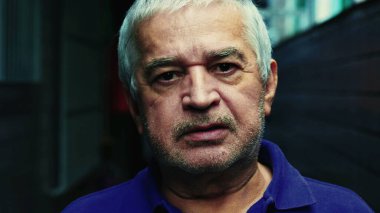 Ciddi, tıraşsız, gri saçlı, buruşuk suratlı, yaşlılığı ve deneyimi resmeden yaşlı bir adamın yakın çekimi.