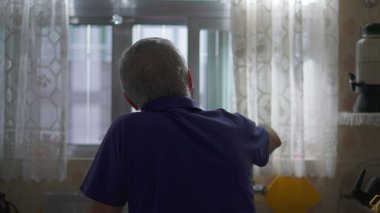Yaşlı bir adam pencereden dışarı bakıyor, eve bakıyor, perdeleri açıyor düşüncelere dalıp dışarı bakıyor.