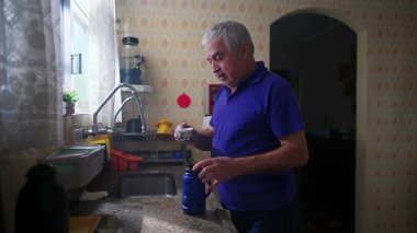 Son sınıf öğrencisi mutfak lavabosunun yanında durup kendine kahve ikram ediyor ve tefekkür ederek pencereden dışarı bakıyor.