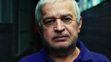 Ciddi, tıraşsız, gri saçlı, buruşuk suratlı, yaşlılığı ve deneyimi resmeden yaşlı bir adamın yakın çekimi.