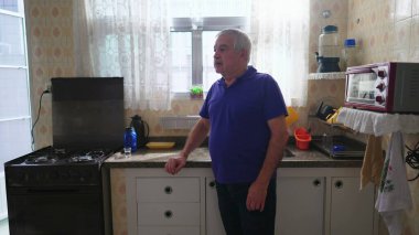 Dalgın yaşlı bir adam mutfağın yanında duruyor derin zihinsel bir yansımayla, düşünüp taşınıyor. Kollarını kavuşturup ikilemde kalan yaşlı kişi