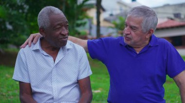 İki farklı kıdemli arkadaş park bankında oturmuş dostluk anlarını paylaşıyorlar. Eski Kafkasyalı arkadaş sohbette Afrika kökenli Amerikalı Colelague 'ın omzunu uzatıyor.