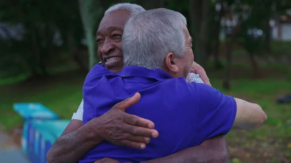 Two diverse friends hugging each other at park. An African American older man embracing a caucasian companion depicting friendship and camaraderie in old age