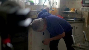 Tıbbi yardıma ihtiyacı olan Kafkasyalı kıdemli erkek, mutfak lavabosunun yanında tek başına kalp krizinden yere yığılıyor.